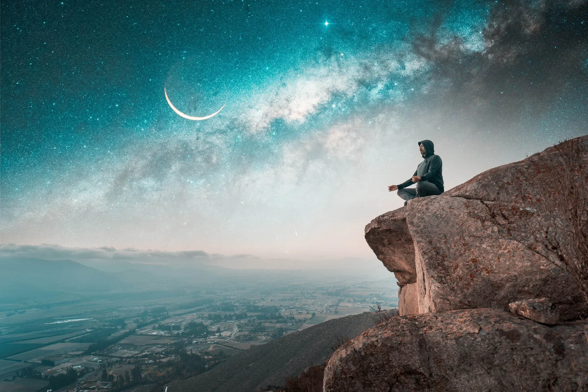 A person sitting cross-legged on a rock formation hills, meditating under a starry night sky with a crescent moon and the Milky Way galaxy visible.